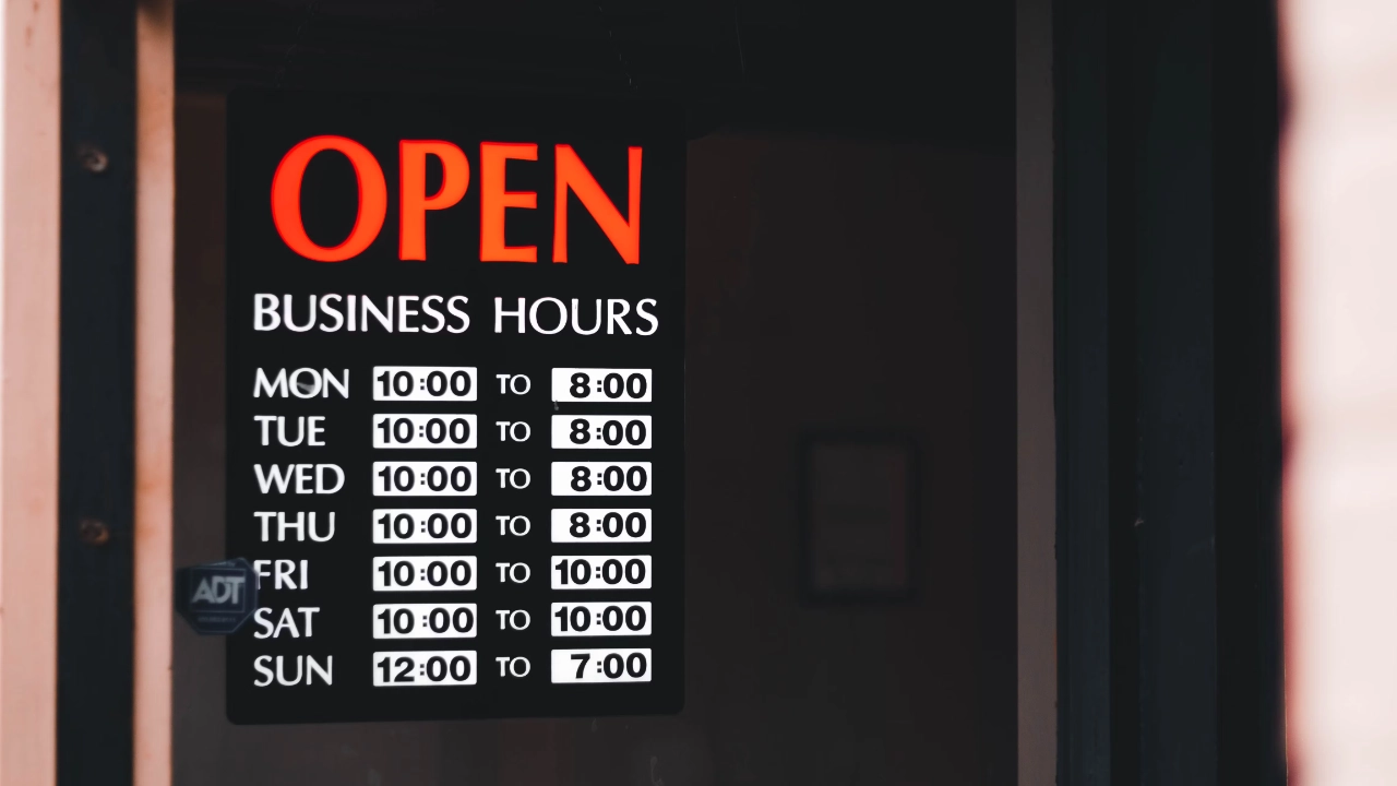 A black business hours open sign hanging on a glass door with red glowing letters, representing a U.S. business presence for an E-1 change of status.