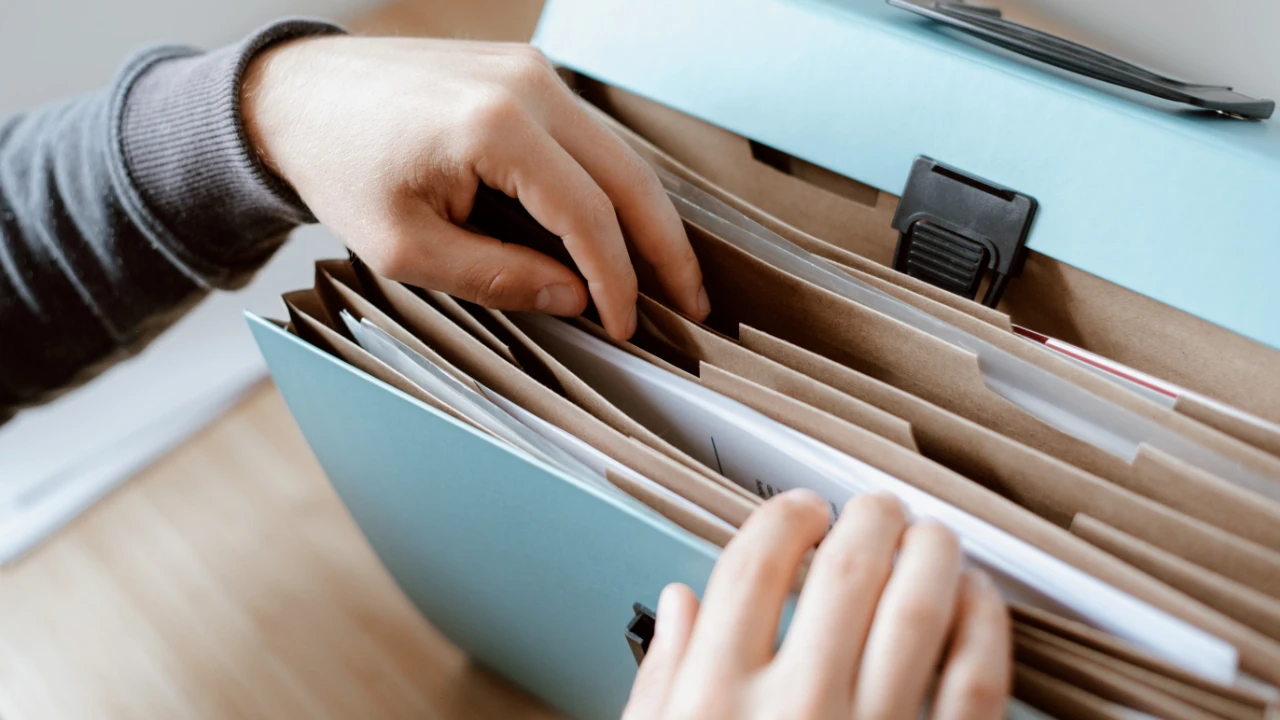 Close-up of a person's hands organizing documents in a blue accordion file folder for an E-2 visa application.