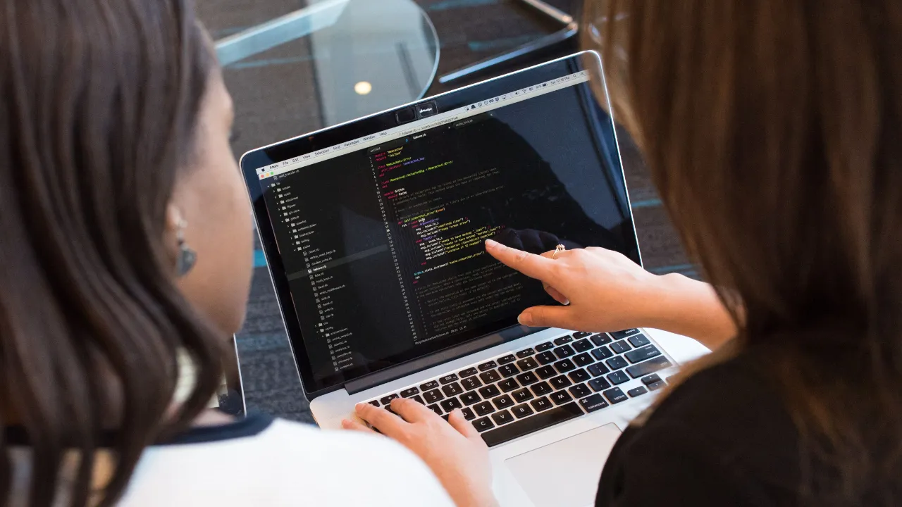 Two individuals reviewing code on a laptop screen in a modern workspace