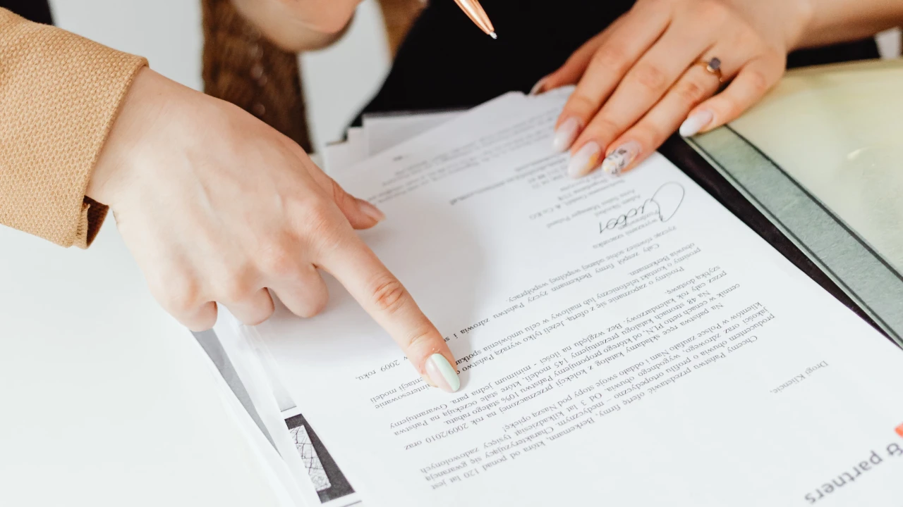 A close-up view of a legal professional pointing at an immigration document and contract on a desk, highlighting key clauses for correction.