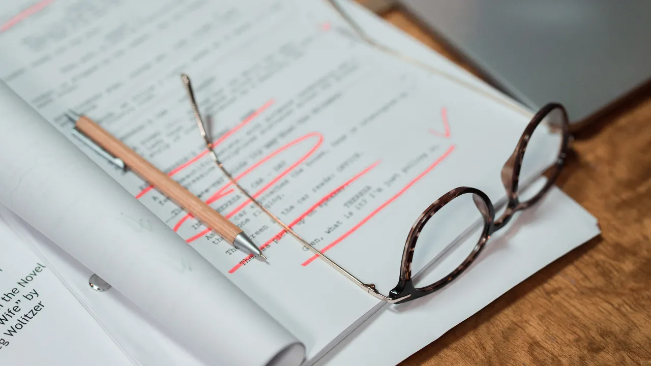 Close-up of legal documents with red edits, a pencil, and reading glasses on a wooden desk, representing a CBP secondary screening review.