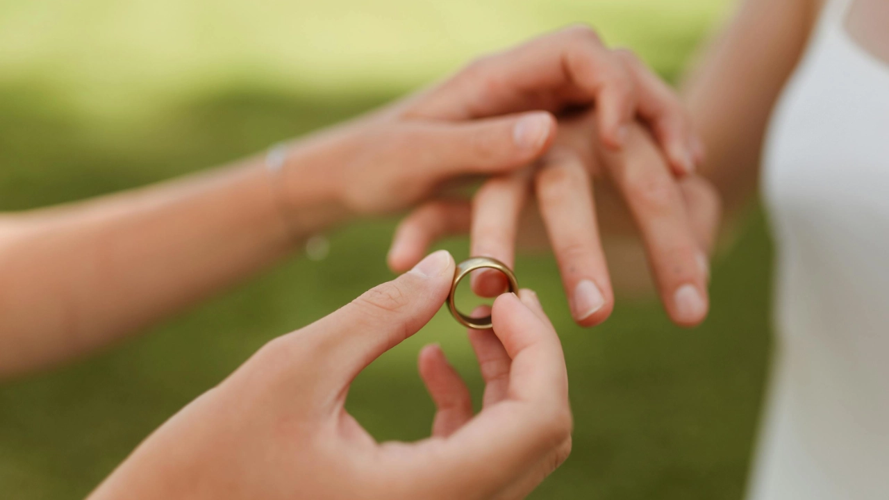 Close-up of one hand placing a ring on another hand with a blurred green outdoor background