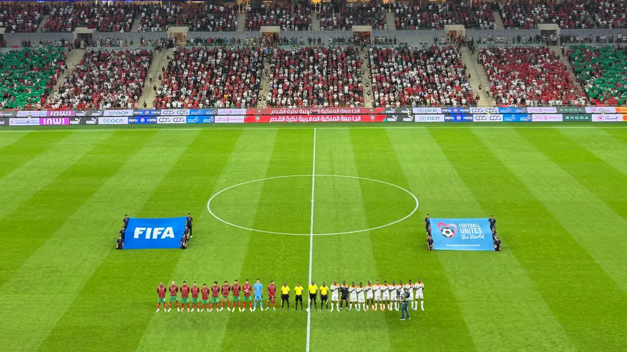 Wide-angle view of a soccer stadium during a FIFA World Cup pre-match ceremony with players lined up on the green pitch and crowds in the stands.