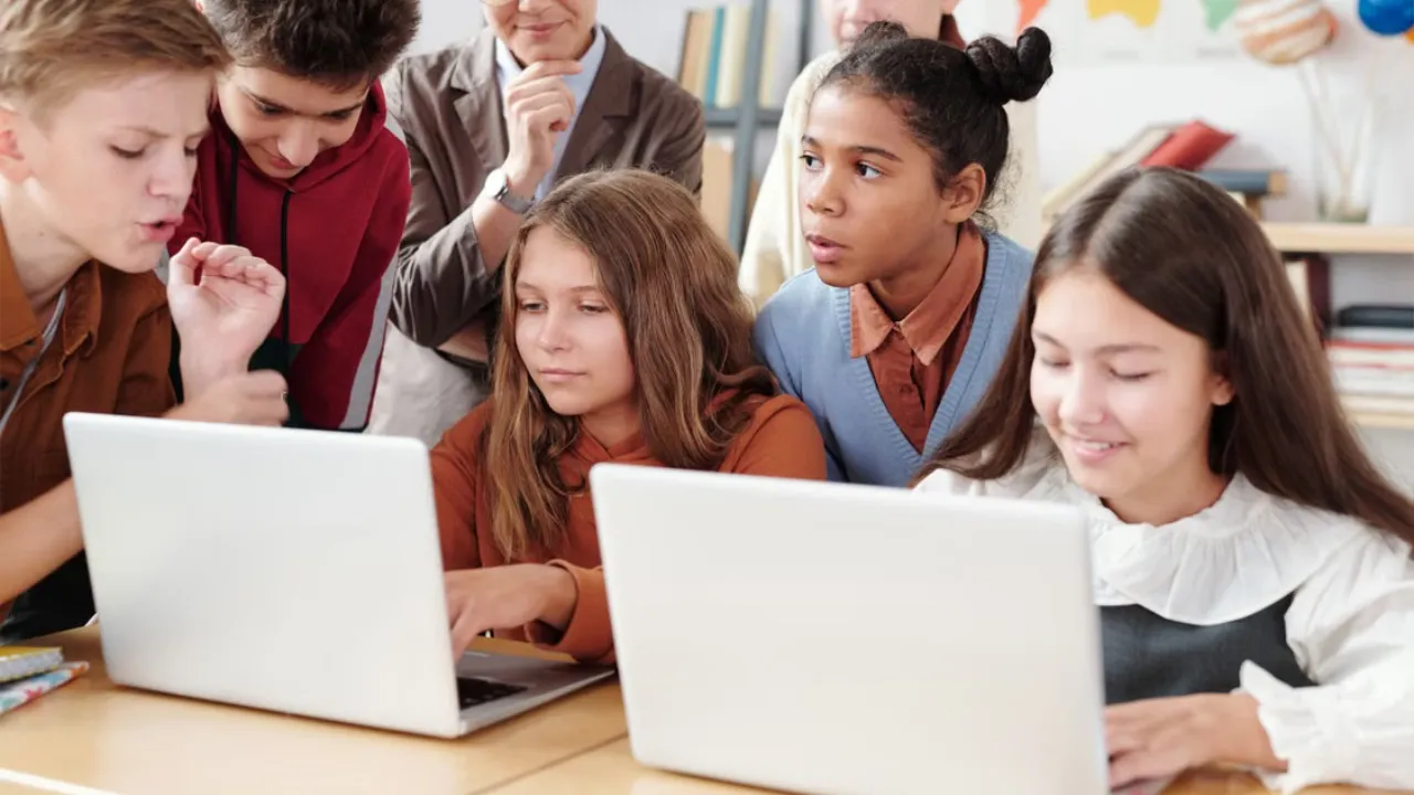 Group of students and an instructor working together on laptop computers during a coding education class.