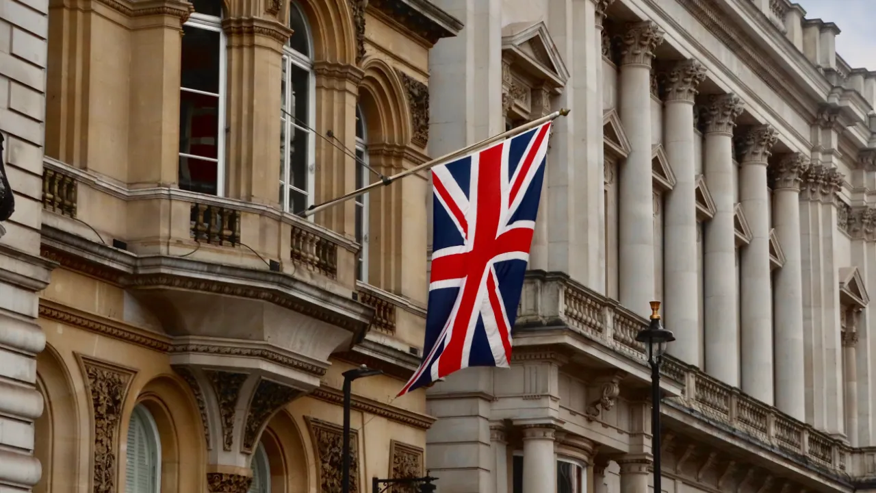 The Union Jack flag flying from a classic stone building facade in London, symbolizing the U.K. inhabitant requirement for British E-2 treaty investor visa applicants.
