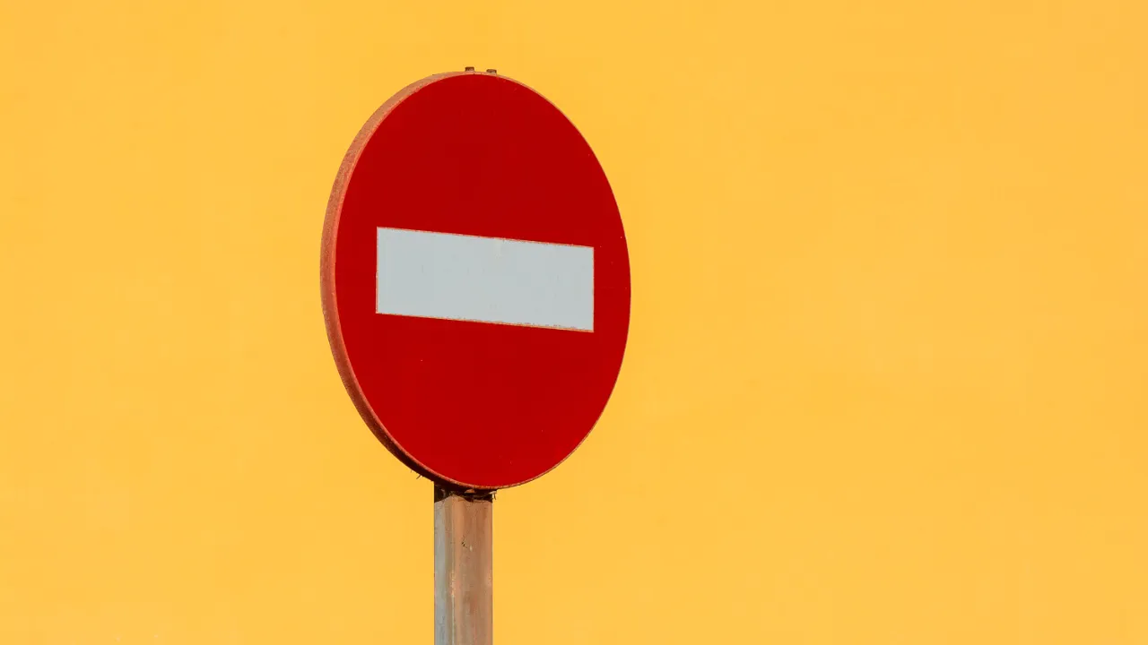 Red no entry road sign against a bright yellow background, representing work and travel authorization revoked by USCIS for green card holders