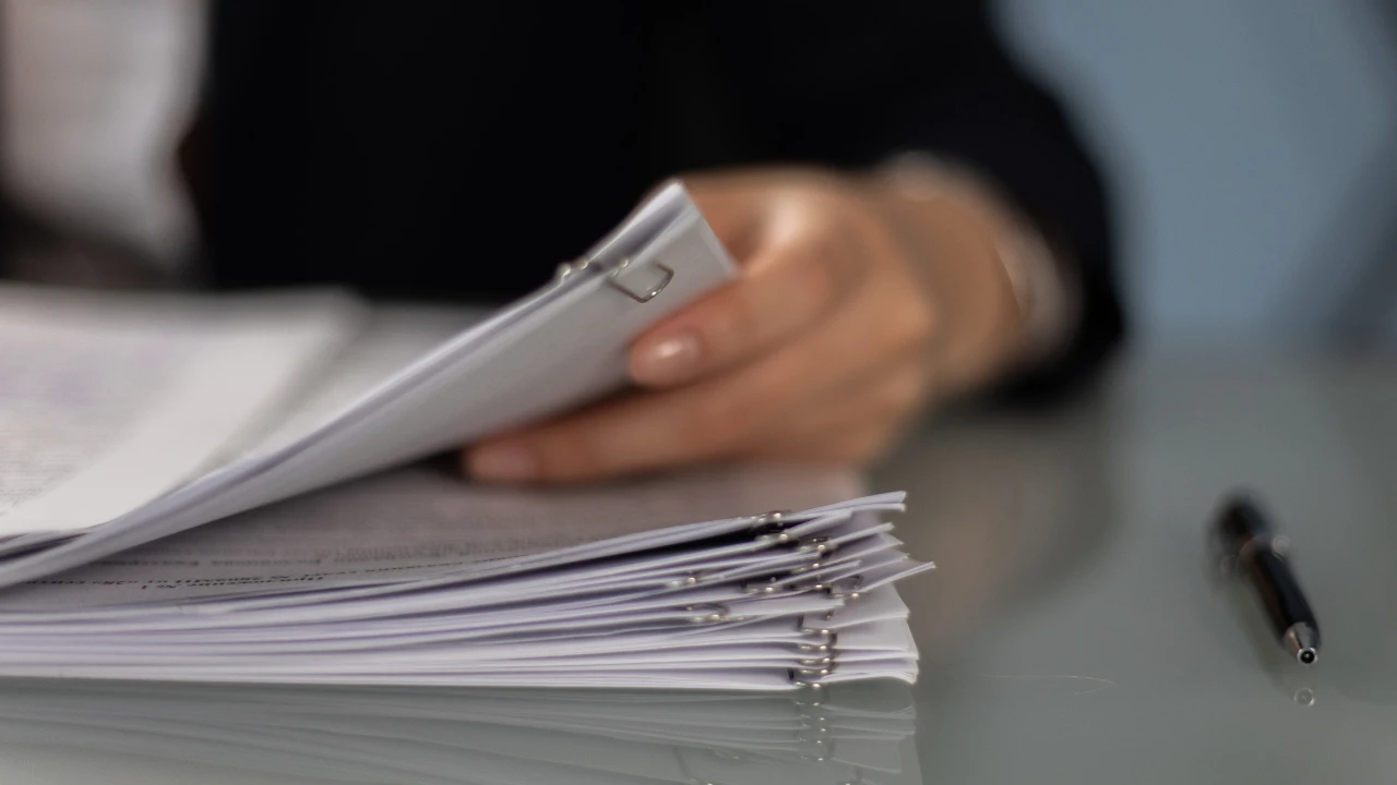 A person reviewing a stack of clipped documents on a desk