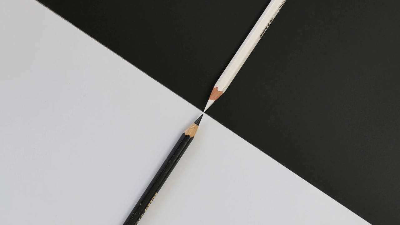 A white pencil on a black background and a black pencil on a white background meeting tip to tip, illustrating the difference between an RFE and a NOID from USCIS.