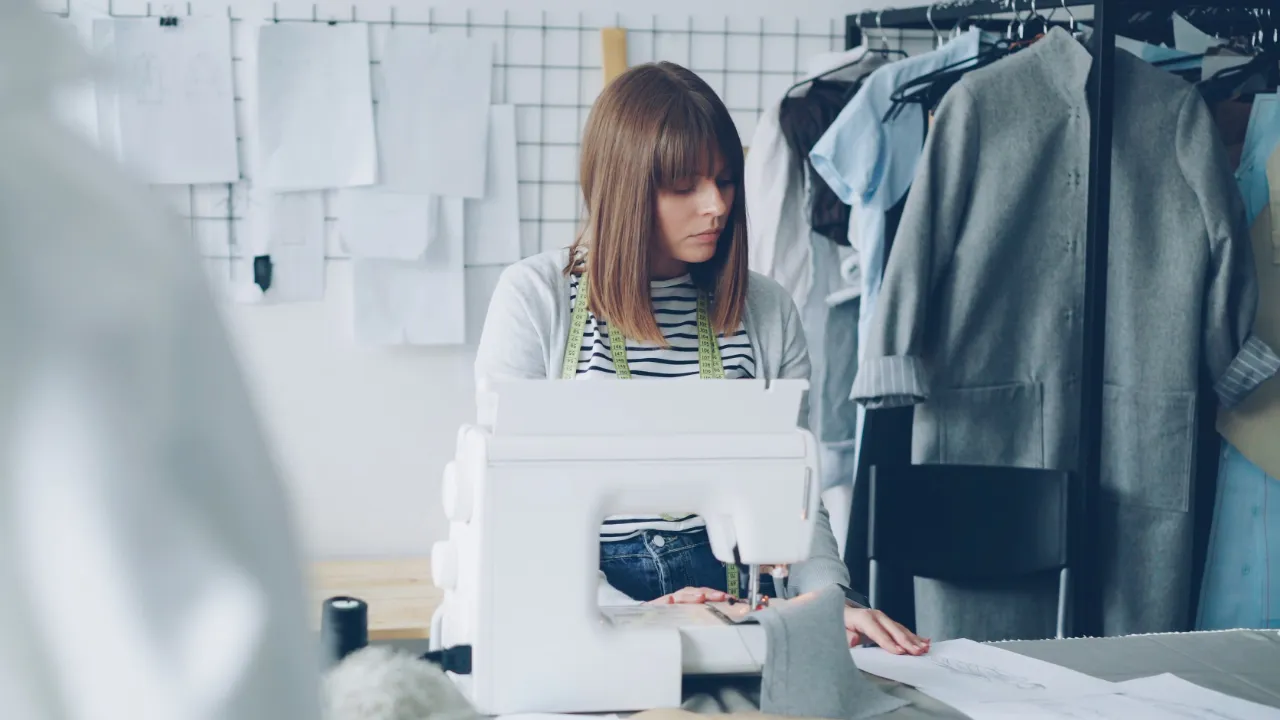 Entrepreneur sewing a garment in her own fashion design studio, representing a startup founder who can sponsor herself for an H-1B visa through her company