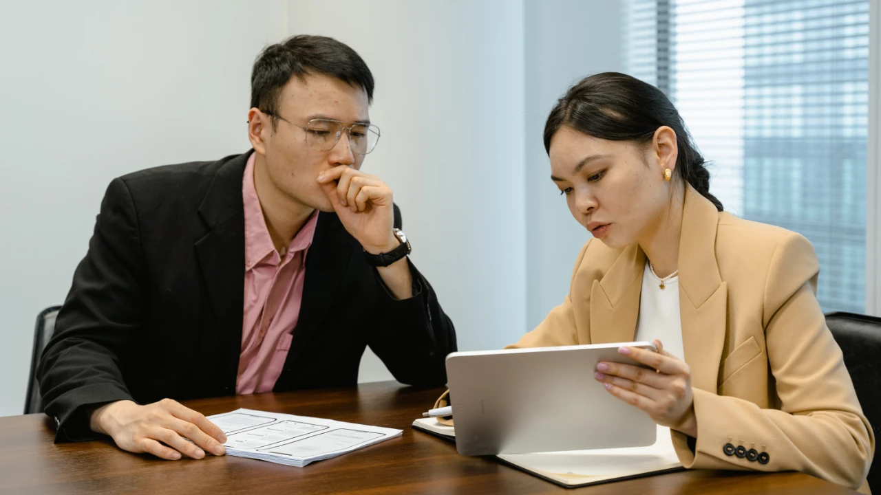 Two business professionals in a meeting room reviewing documents and a tablet, representing a TN Management Consultant case discussion