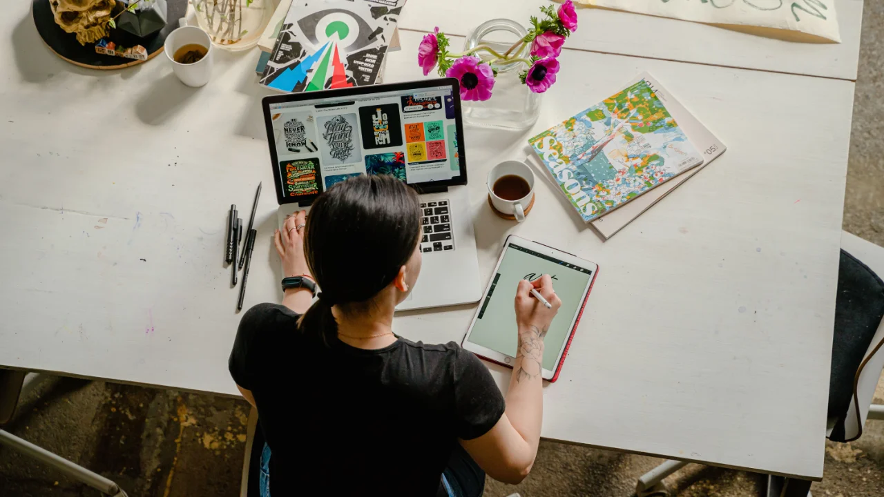 Graphic designer working on lettering at a laptop and tablet workspace, illustrating an approved EB-3 PERM I-140 petition for a designer in California