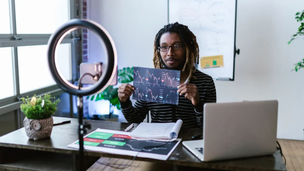 Independent news creator filming a market analysis segment with a ring light while holding printed financial charts, illustrating I visa questions for social media news channels