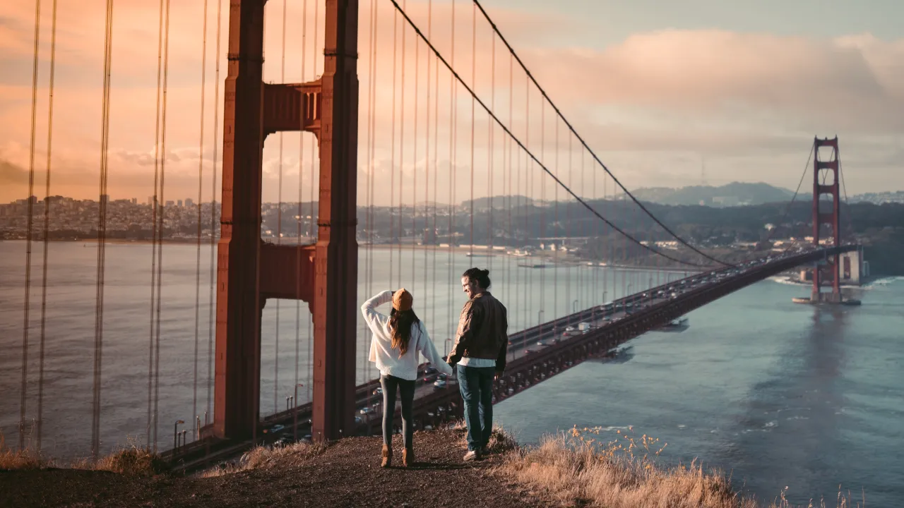 A couple holding hands on a hillside overlooking the Golden Gate Bridge at sunset after the foreign fiancé entered the United States