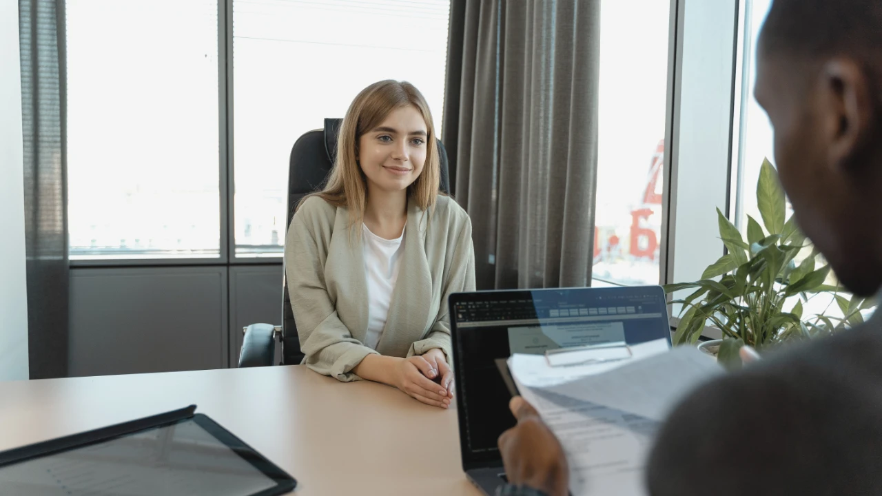 Job applicant seated across a desk from an interviewer reviewing a résumé and laptop, representing an employer assessing PERM experience with the same employer.