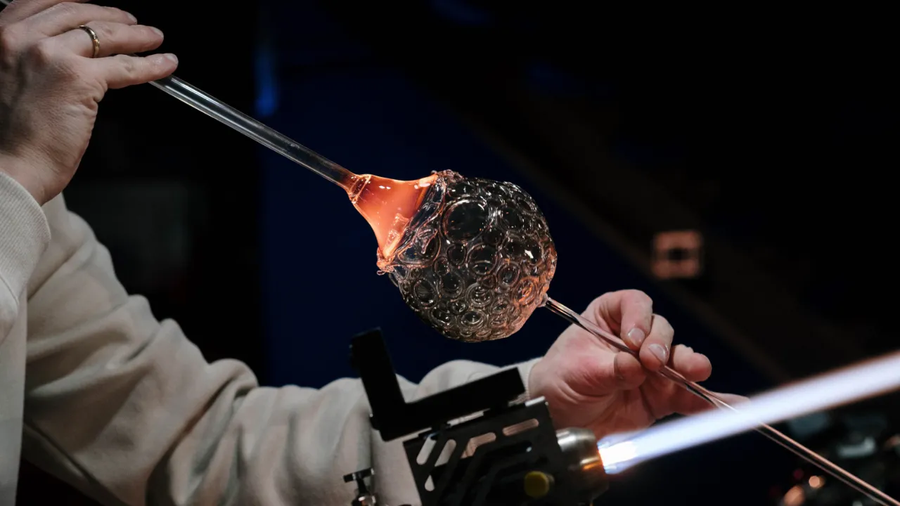 Artisan's hands shaping a textured glass sphere over a torch flame
