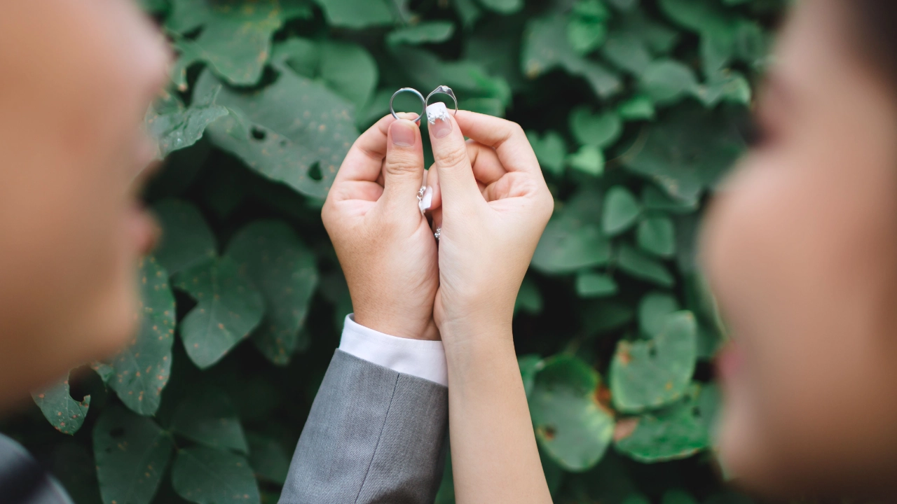 A couple holding two wedding rings, representing a marriage-based green card approved by USCIS.