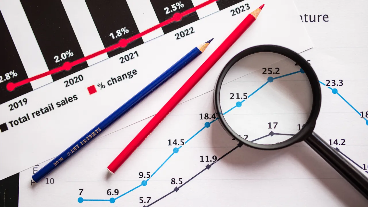 Charts under a magnifying glass, representing E-2 business plan projections reviewed at visa renewal