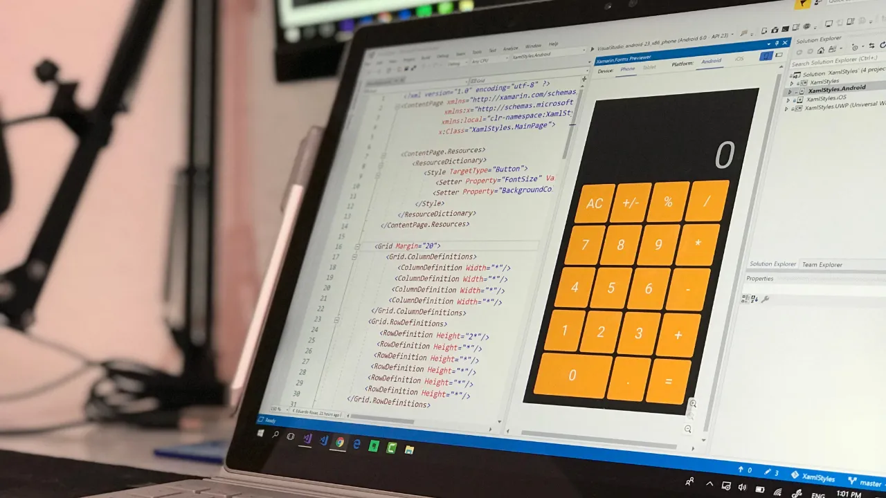 Laptop screen showing mobile app code in a development environment beside a live preview of an orange calculator app on a phone layout.
