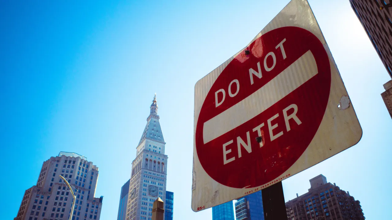 Red and white Do Not Enter road sign against a blue sky with Manhattan high-rise buildings behind it