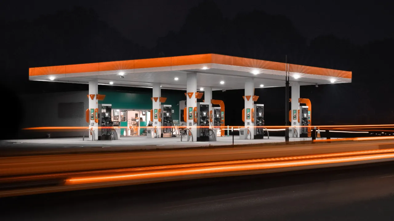 Gas station forecourt and convenience store lit up at night, with light trails from passing traffic, representing an existing business purchased for an E-2 visa.
