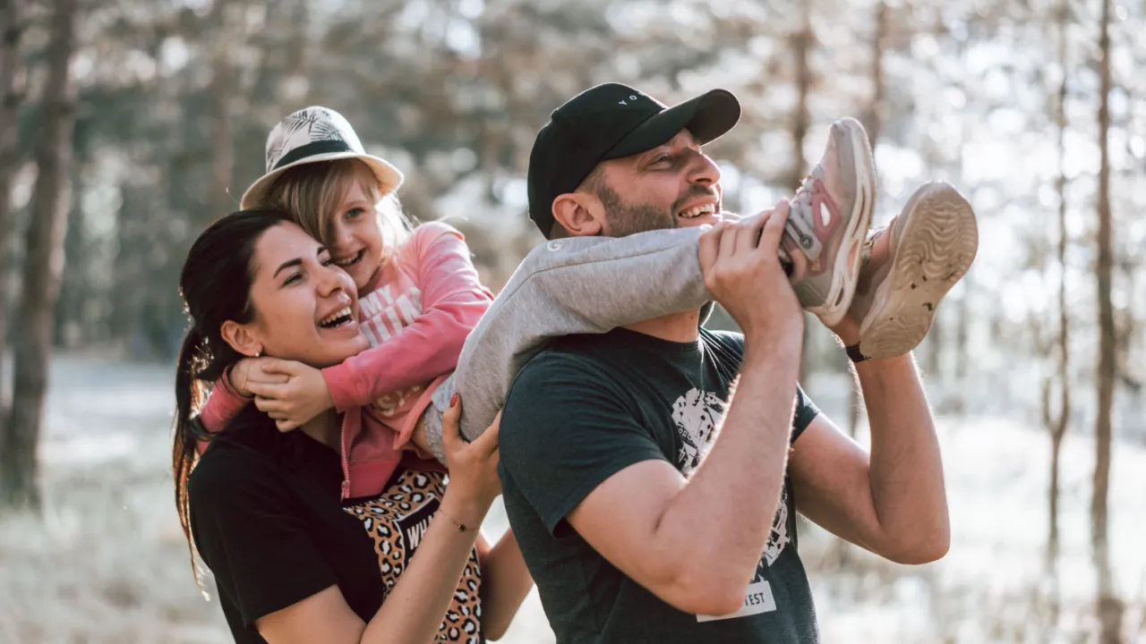 Smiling couple carrying their young daughter on a walk through a sunlit forest