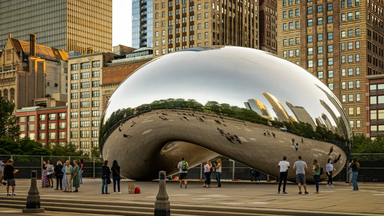 Visitors gathered around a large reflective steel sculpture in a city plaza surrounded by high-rise buildings